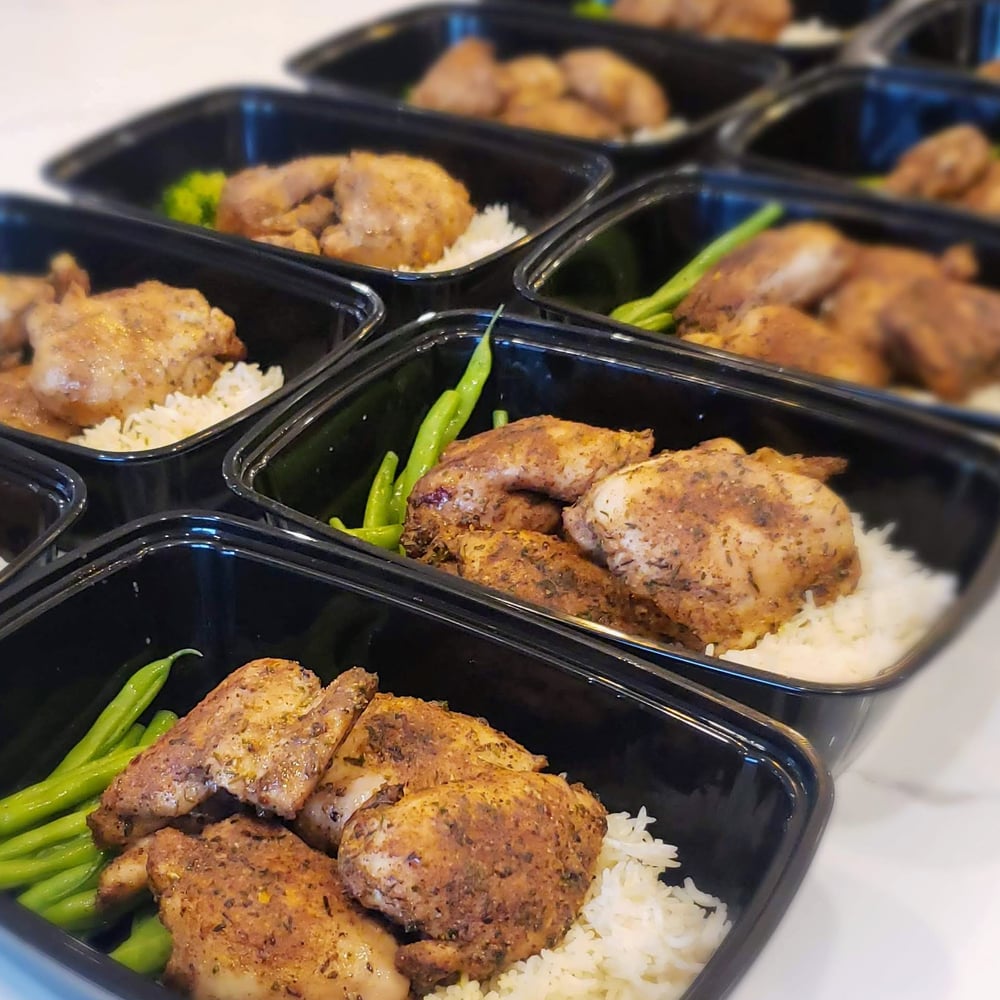 Our personal chef prepared jerk chicken with coconut rice and green beans, meal prepped and divided into single serving containers. The 10 single serving meal containers are displayed on the white counter top in 2 rows. Rice on the bottom, topped with jerk chicken to the right and green beans to the left.